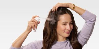 A smiling woman applies Native Dry Shampoo, a powder dry shampoo, to her roots, demonstrating how to use dry shampoo correctly for oily hair without leaving white residue, making it the best dry shampoo for everyday use