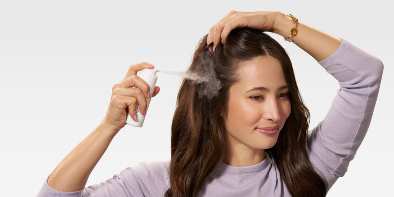 A smiling woman applies Native Dry Shampoo, a powder dry shampoo, to her roots, demonstrating how to use dry shampoo correctly for oily hair without leaving white residue, making it the best dry shampoo for everyday use