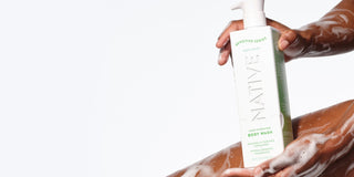 A person with dark skin holding a bottle of Native Sensitive Series Hydrating Body Wash, with visible suds on their arm, demonstrating how a moisturizing body wash for sensitive skin can help maintain the skin barrier and prevent dry skin