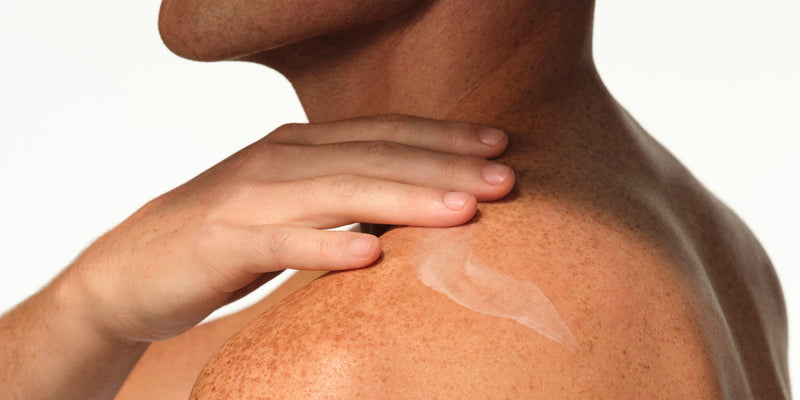 A person with freckled skin applying a white body cream to their shoulder, demonstrating a body care routine for sensitive skin using Native Sensitive Series body lotion