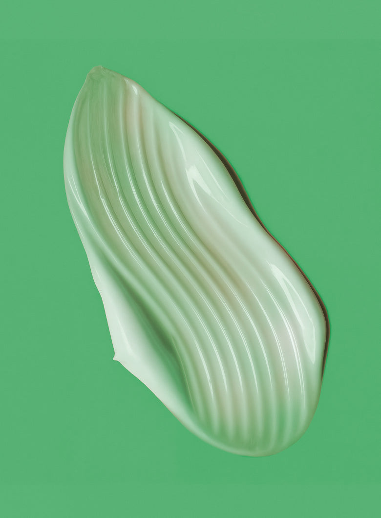 A single glossy, wavy-edged cosmetic smear or droplet in a pale mint green shade, set against a solid medium green background.
