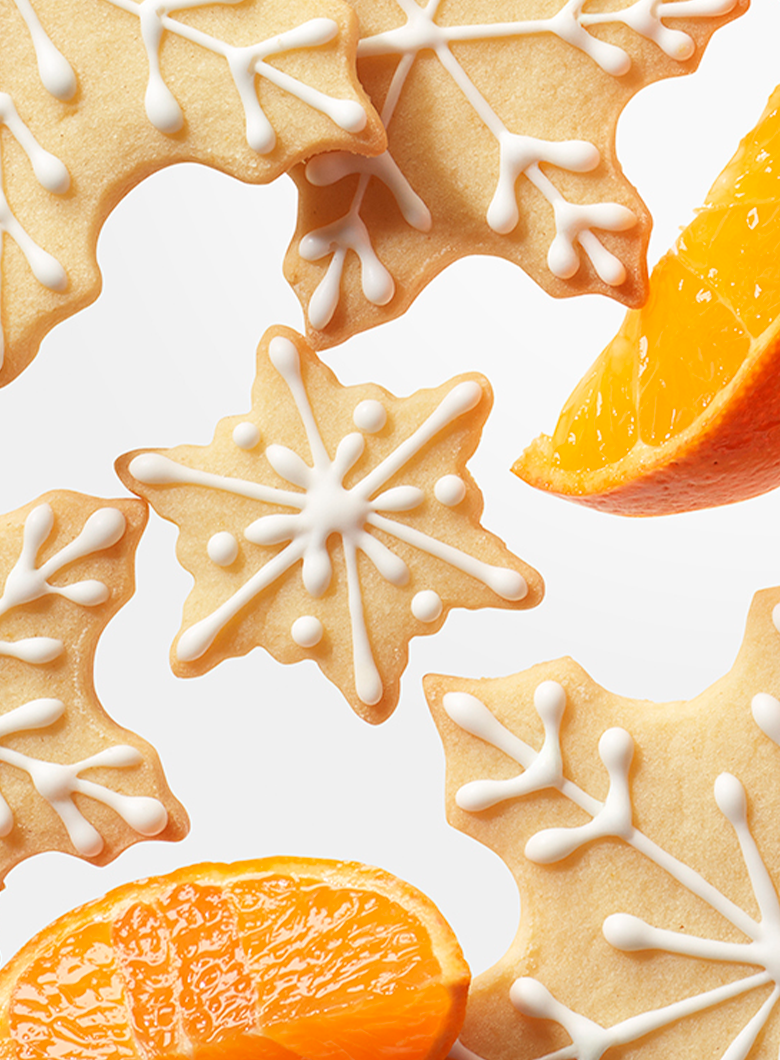 Decorated gingerbread cookies shaped like snowflakes, arranged with orange slices on a clean white background.