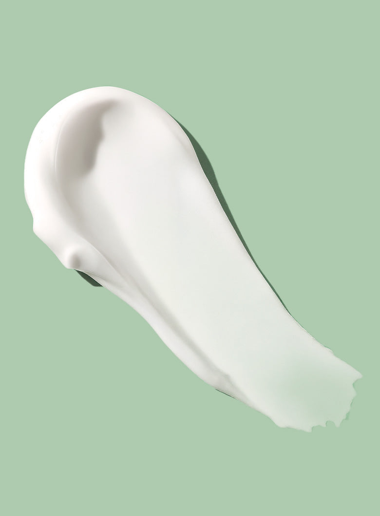 A thick, creamy white cosmetic lotion displayed diagonally against a solid light green background.