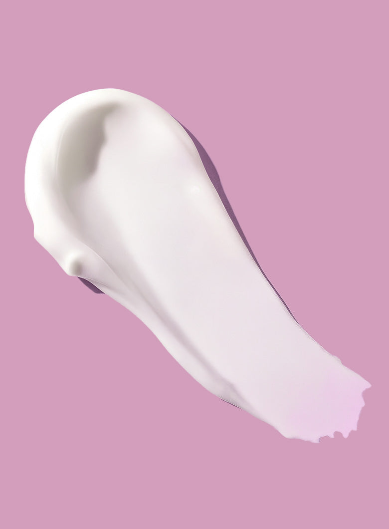 A thick, creamy white product swatch, like a lotion, spread in a diagonal smear on a solid pink background.