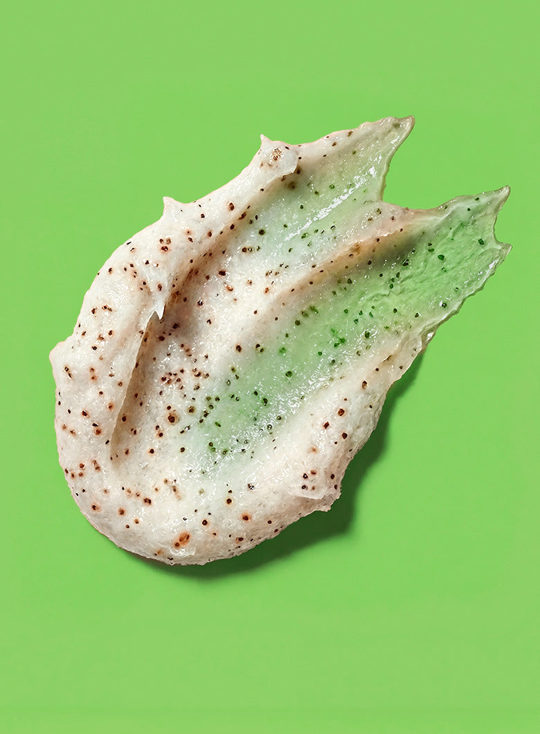 A dollop of textured cosmetic cream or clay mask showing a dual-tone color story: a creamy off-white base speckled with brown, and a translucent light green section with green flecks, set against a solid bright green background.