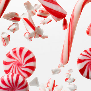 Red and white striped peppermint candies, including whole candy canes and round swirled peppas, floating and breaking into pieces against a clean white background.