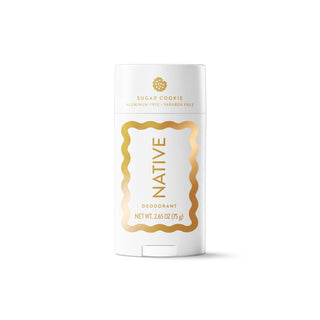 A white Native brand deodorant stick in the Sugar Cookie scent, featuring elegant gold typography and a gold wavy border frame on a clean white background.