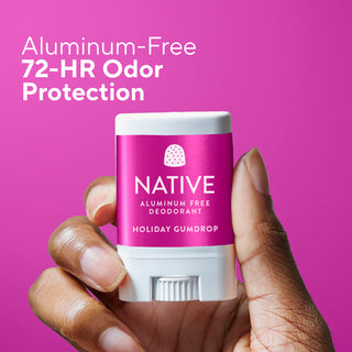 Hand holding a Native aluminum-free deodorant stick with pink label on a pink background