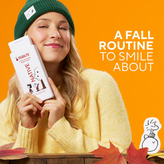 A woman in a green beanie and yellow sweater holds a white Peanut body wash package against her face against a bright orange background, with the text 'A FALL ROUTINE TO SMILE ABOUT' and autumn leaves at the bottom.