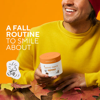 A smiling man in a yellow sweatshirt and red beanie holds a jar of Native Peanut Butter Co. Maple Latte Peanut Butter against a bright orange background with the text 'A FALL ROUTINE TO SMILE ABOUT' and autumn leaves at the bottom.