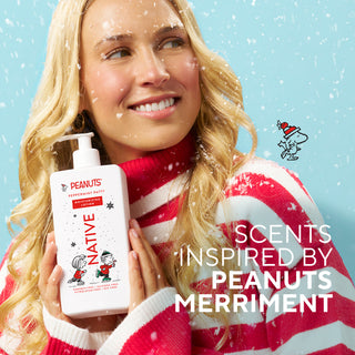A smiling blonde woman in a red-and-white striped sweater holds a bottle of Peanuts-themed peppermint soap against a light blue snowy background. The bottle is labeled 'Peanuts Native Peppermint' and the image includes the text 'SCENTS INSPIRED BY PEANUTS MERRIMENT' and a small Snoopy graphic.