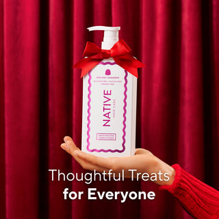 A hand in a red knit sleeve holds a white pump bottle of Native Hair Care Holiday Cheerful hair care treatment with a red ribbon bow, set against a red curtain background with the text 'Thoughtful Treats for Everyone'.