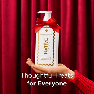 A hand in a red knit sleeve holds a white pump bottle of Native Hair Care Sweetening Conditioner against a red curtain backdrop, with a red ribbon bow tied around the neck and the text 'Thoughtful Treats for Everyone' at the bottom.