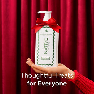 A hand in a red knit sleeve holds a white pump bottle of Native Hair Care hand care with a red ribbon bow, set against a red curtain background with the text 'Thoughtful Treats for Everyone'.