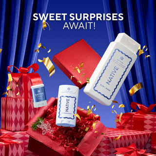 Native Essentials body wash and deodorant products displayed with red gift boxes, ribbons, and gold confetti against a blue curtain backdrop, with the text 'SWEET SURPRISES AWAIT!'.